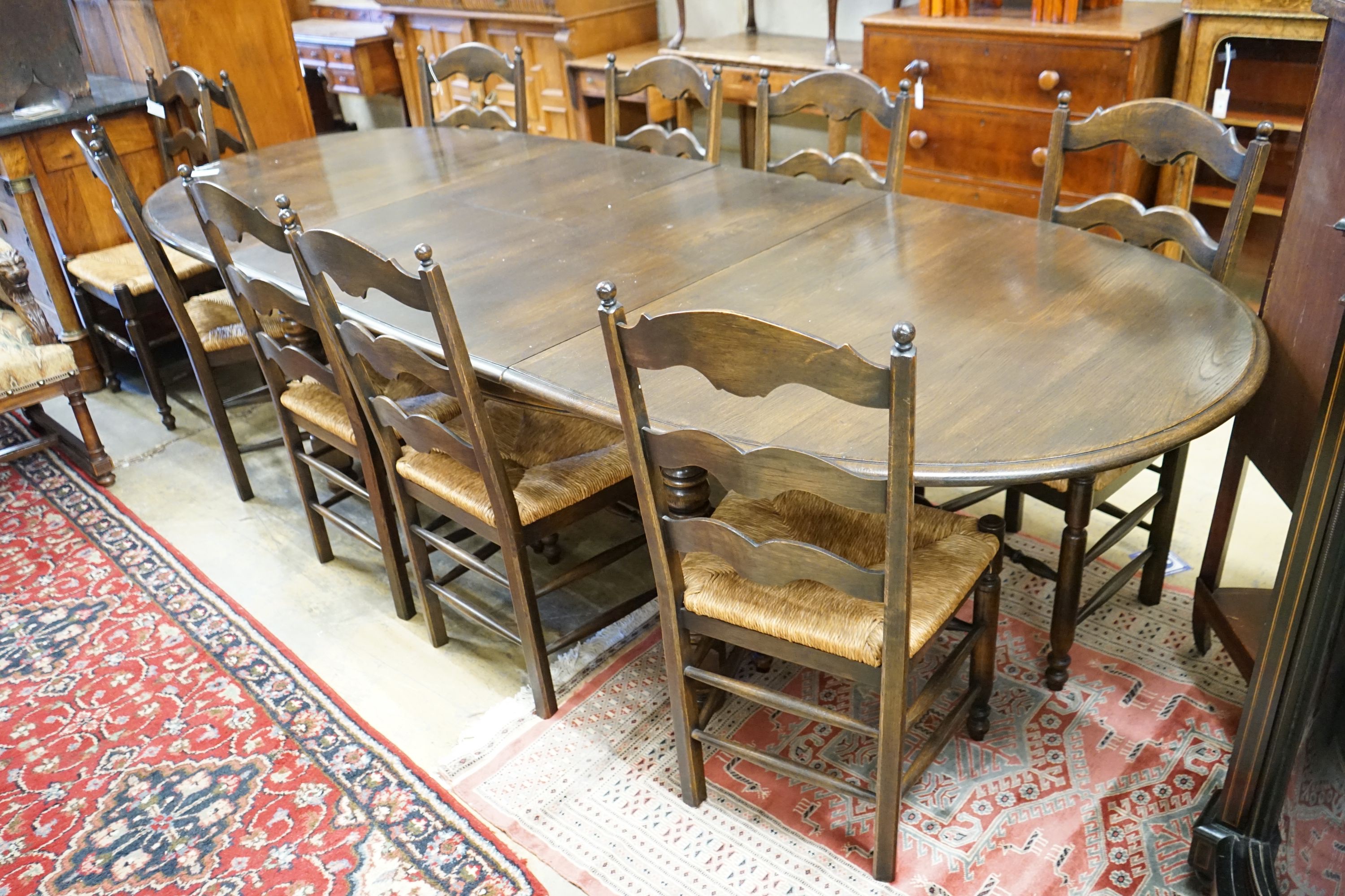 A French style oak extending dining table, with two spares leaves, 280cm extended, width 11cm, height 74cm together with a set of ten ladder backed rush seated chairs